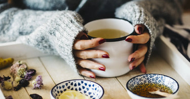 Hands holding a warm cup of tea with herbs and honey