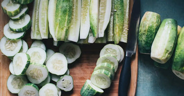 Peeled and sliced fresh cucumbers on a cutting board.
