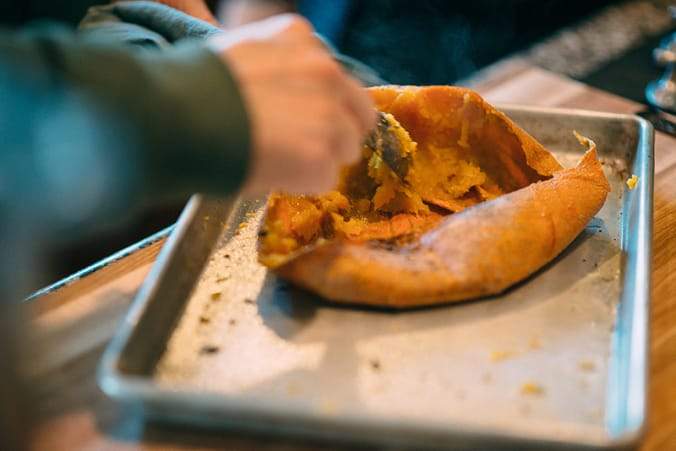hand with spoon scrapping inside from pumpkin half on baking pan
