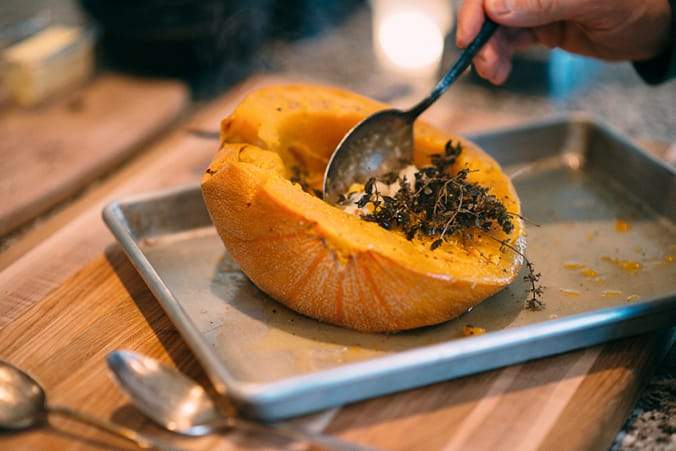 Scooping soft insides mixed with herbs out of pumpkin half.