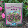 Box of Down to Earth All Natural Fertilizer Rose & Flower Mix in a garden with pink flowers.