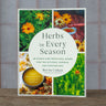 Herbs in Every Seaon guide book with bright herb photos on cover sitting on wooden table.