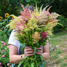 Gardener holding bright plumes of yellow and pink celosia flowers with a green background.